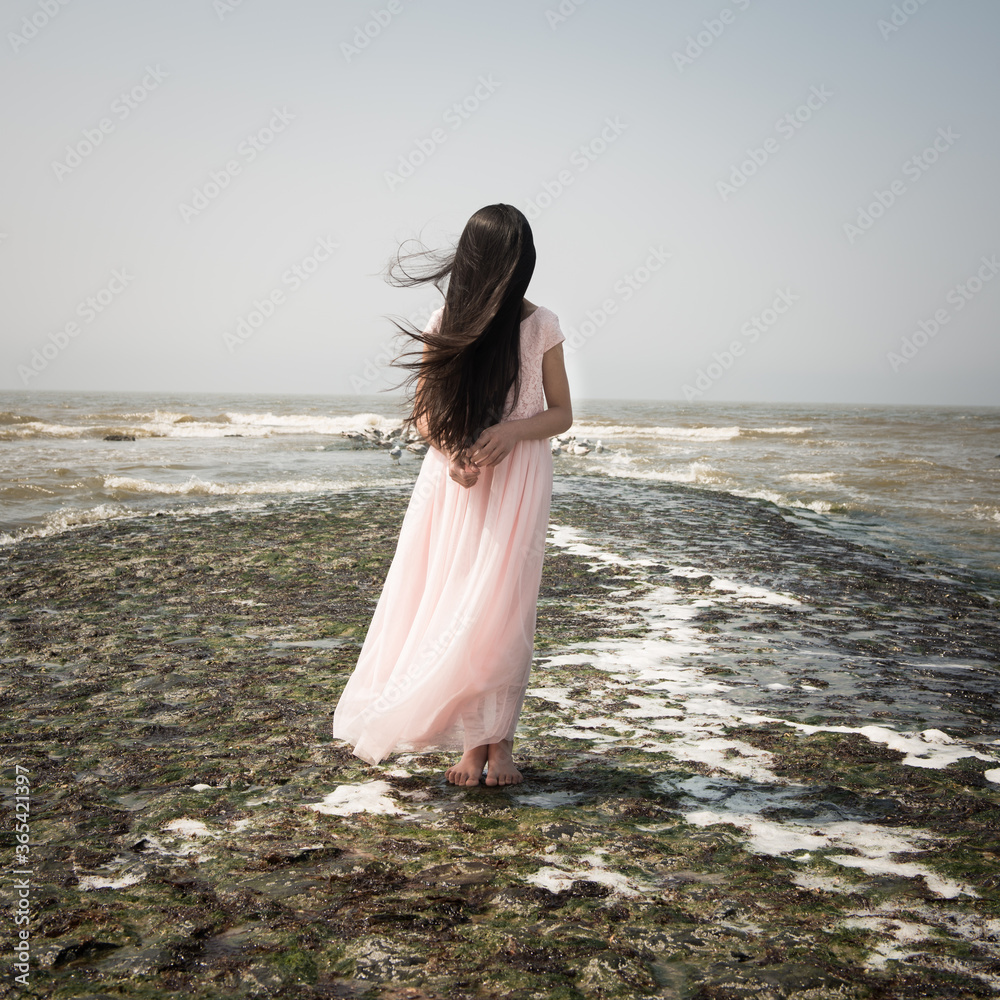 Teenage girl covering her face with long hair while standing on beach ...