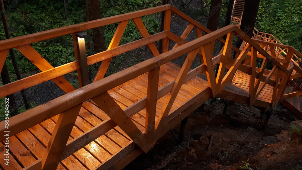 wet wooden stairs, wooden bridge in the rain in the evening is illuminated by beautiful light from lanterns, glare from a lantern on a wet tree