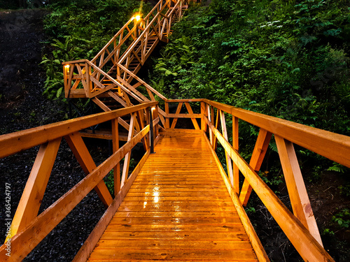 wet wooden stairs, wooden bridge in the rain in the evening is illuminated by beautiful light from lanterns, glare from a lantern on a wet tree
