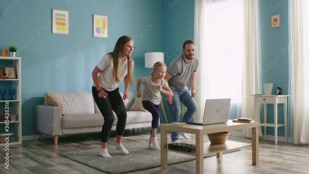 Father, mother, and their small daughter dance together, having fun at home, use online application, video, to practice dancing, enjoying their common hobby, Slow motion. Father, mother, and their small daughter dance together, having fun at home, use online application, video, to practice dancing, enjoying their common hobby, Slow motion.