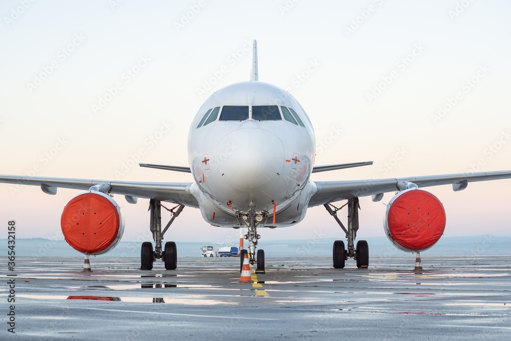 Obraz premium Front view of white airplane. Jet commercial aircraft on airport apron, morning daylight sky, puddles after rain. Modern technology in fast transportation, private business travel, charter flight.