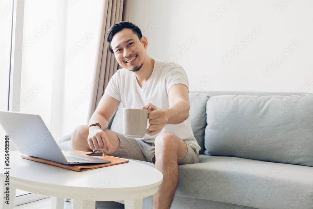 Happy Asian man is working on his laptop in the living room.
