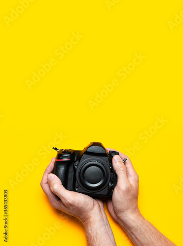 Modern SLR and mirrorless camera in male hands on yellow background flat lay copy space. Digital photography, body without lens, photographer's technique, digital camera, professional photo camera