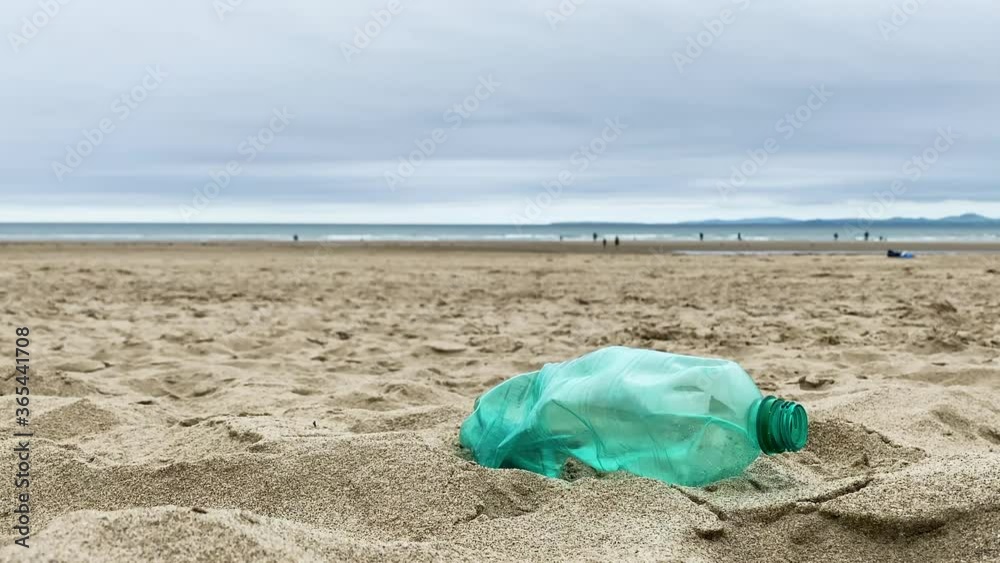 An empty green plastic bottle discarded on a beach. Coastal pollution An empty green plastic bottle discarded on a beach. Coastal pollution