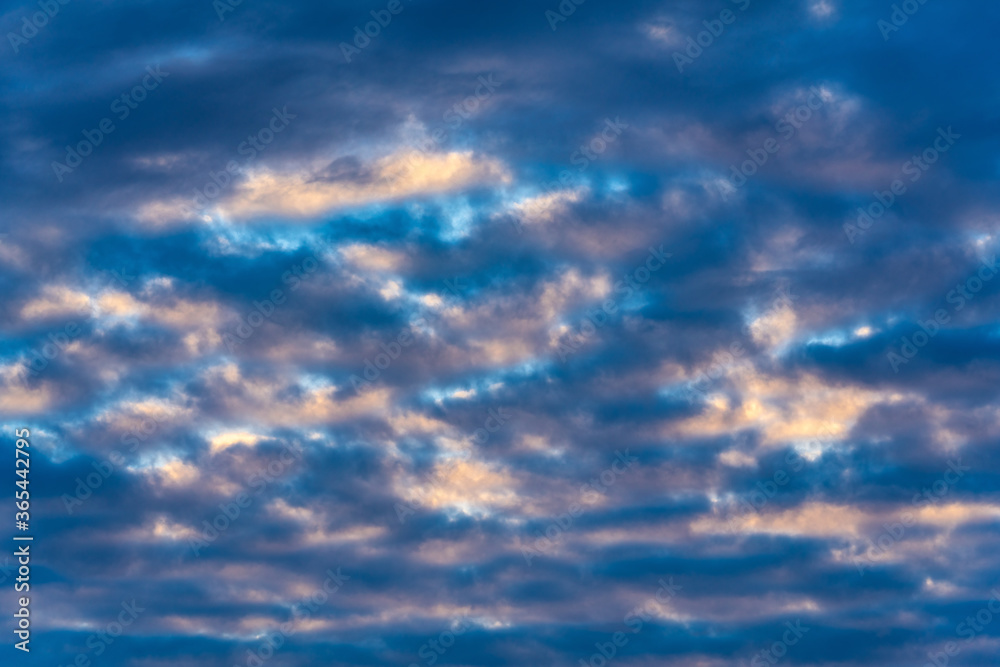 Dramatic clouds in blue sky, illuminated by rays of sun at sunset to change summer weather. Soft focus, motion blur multicolored cloudscape background.