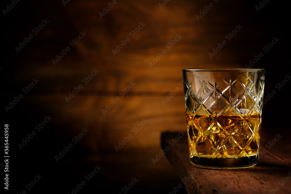Half a glass of whiskey with ice cubes on an old wooden table, rustic style