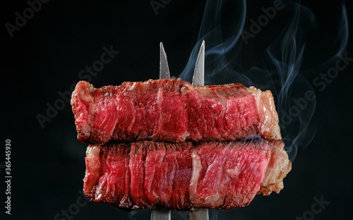 Sliced and steaming rare rib eye steak on a fork on a dark background, close up