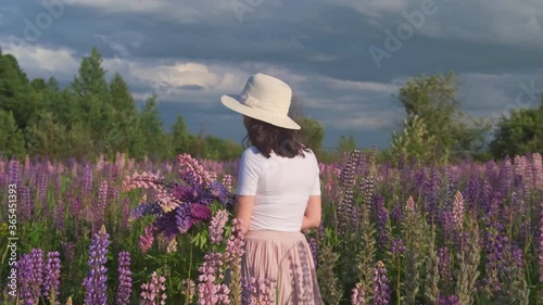 A beautiful woman in a hat and skirt with a bouquet of wild flowers walks through a field with purple lupines Bluebonnet flowers.
