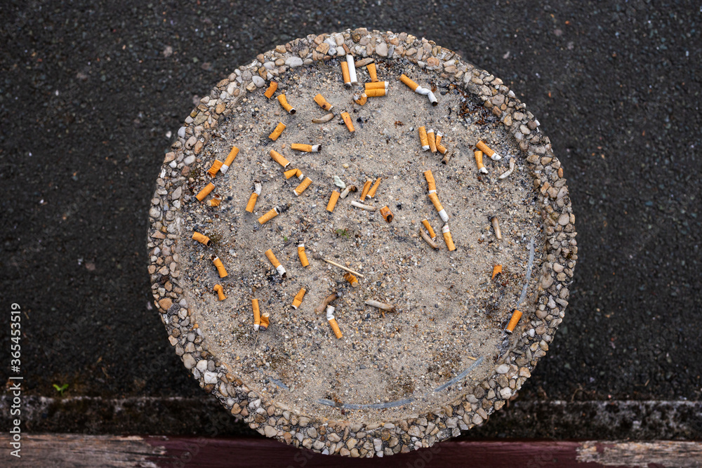 top of a cigarette ashtray outdoor, smoke area, top view, big round ashtray with sand in public place, full of cigarette butts