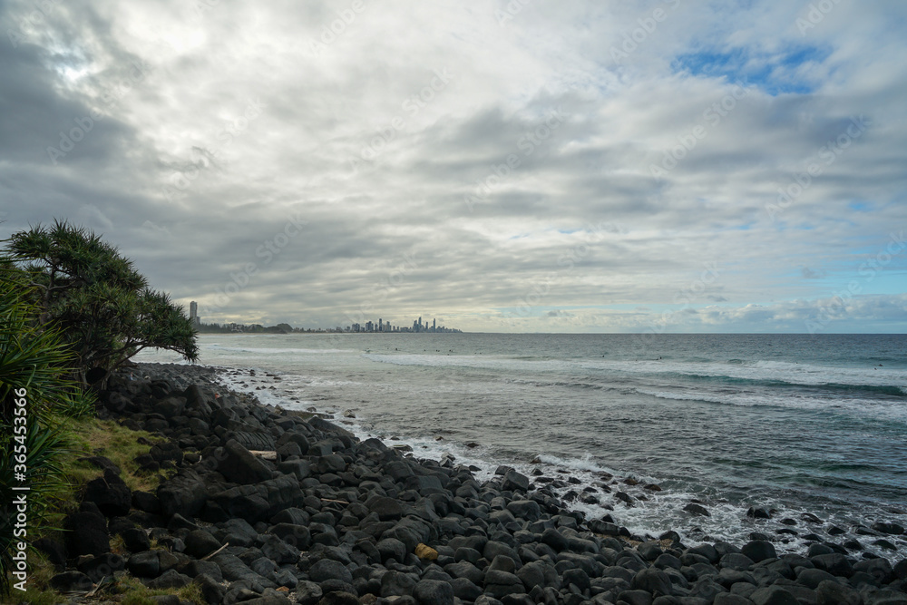 Rocky shoreline with rain clouds over the sea at Burleigh Heads, with Surfers Paradise city skyline on the horizon. Gold Coast, Queensland, Australia.