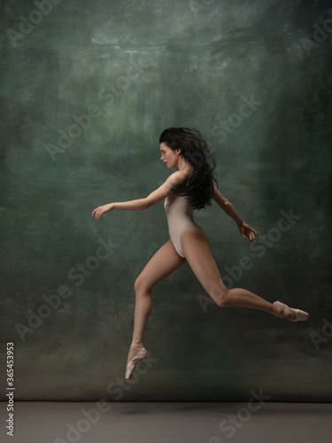 Coming on. Graceful classic ballerina dancing on dark studio background. Pastel bodysuit. The grace, artist, movement, action and motion concept. Looks weightless, flexible. Fashion, style.