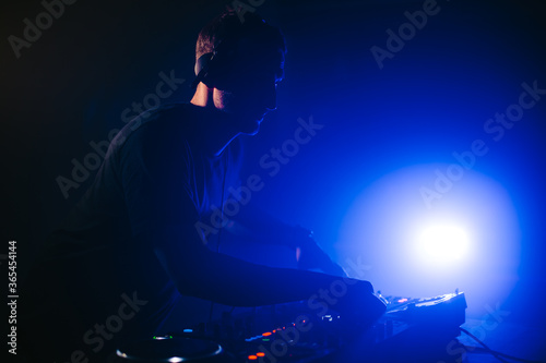 DJ spinning in a night club at a party with dark blue lights.
