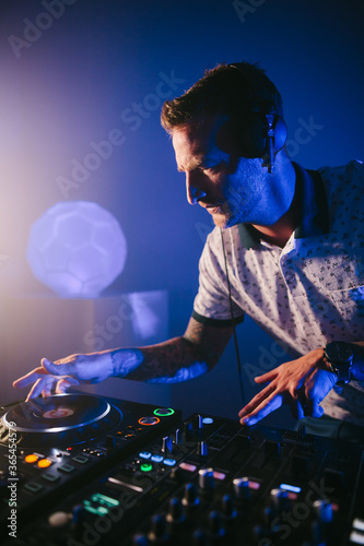 Vertical view of a Techno young Caucasian male DJ with his mixer board playing music at a concert hall at night close up.