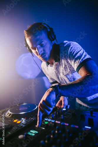 Vertical view of a Techno young Caucasian male DJ with his headphones playing music at a concert hall at night close up.