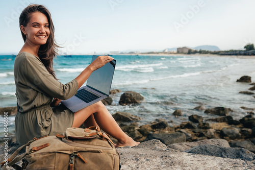 Young female freelancer working on a laptop while traveling by the sea, remote work concept. Work by the sea. Using modern technology, the Internet for communication