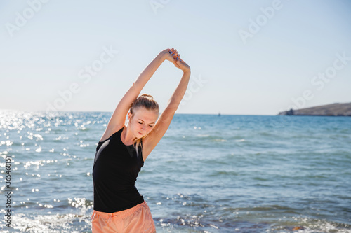 A blonde girl in a dark t shirt and light shorts does sports in the summer on the sea coast