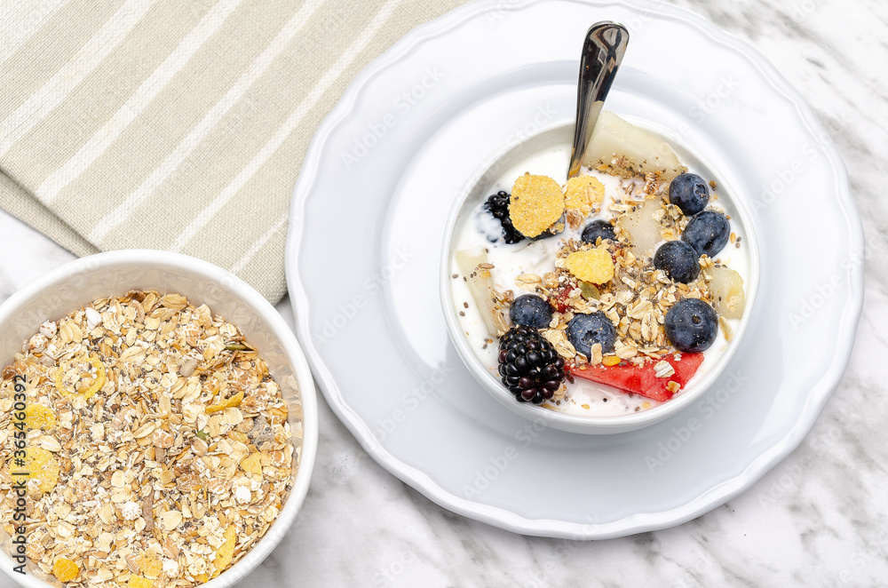 Yogurt bowl with blueberries, red berries and melon. In the background, bowl with cereals. Yogurt bowl with blueberries, red berries and melon. In the background, bowl with cereals.