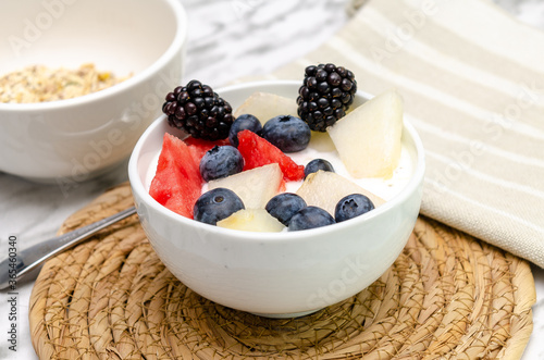 Fototapeta Naklejka Na Ścianę i Meble -  Yogurt bowl with blueberries, red berries and melon. In the background, bowl with cereals.