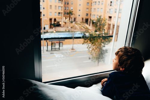 Sad and melancholic boy looks through a window in his apartment during his confinement photo