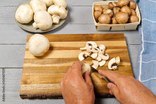 Man hands cuttind fresh champignon mushrooms. White and brown champignon on grey wooden table sliced champignons.