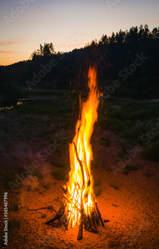 Midsummer Ligo celebration. Huge bonfire on the river shore. Scenic landscape of forest. Sunset sky. Drone view.