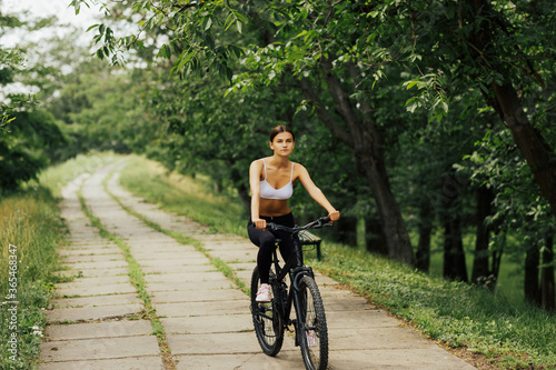 Woman riding a bicycle at the nature. Smiling young model posing while riding bike on the road in summertime. 
