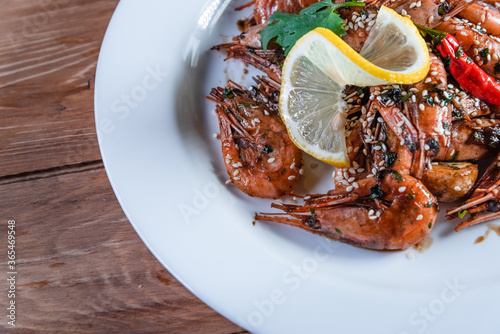 Appetizing fried shrimp with specialties, sesame seeds and lemon, on a white plate on a background of wood. Food concept in restaurants and bars
