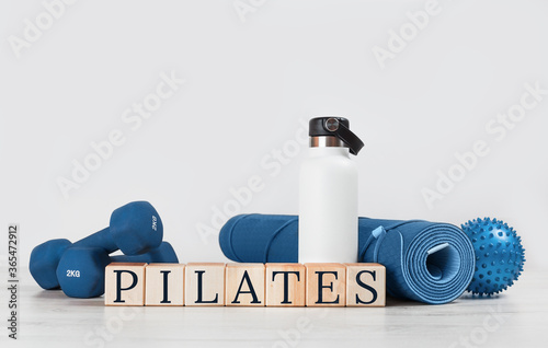 PILATES text. Rolled blue yoga mat and excersise resistance band dumbbells on grey wooden surface. Gender neutral fitness and exercise concept with copy space. Active lifestyle. Workout at home or gym photo