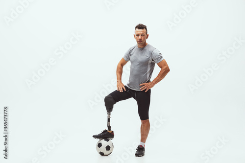 Fototapeta Naklejka Na Ścianę i Meble -  Athlete with disabilities or amputee on white studio background. Professional male football player with leg prosthesis training in studio. Disabled sport and healthy lifestyle concept. Achievements.