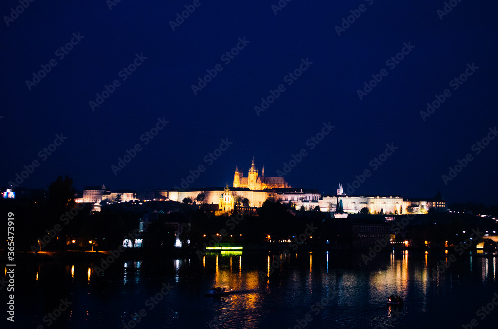 An early evening in Prague during autumn with incandescent lights illuminating the city and reflections over the Vltava river. An early evening in Prague during autumn with incandescent lights illuminating the city and reflections over the Vltava river.
