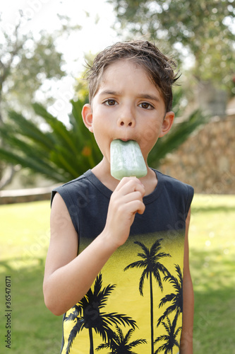 Bambino biondo dai tratti misti europei e brasiliani si gusta un buonissimo ghiacciolo alla menta , sullo sfondo un prato  verde photo