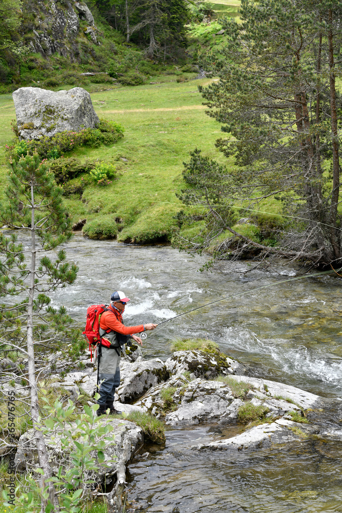 Obraz premium fly fisherman trout fishing with a hiking backpack and an orange jacket in the high mountains in summer