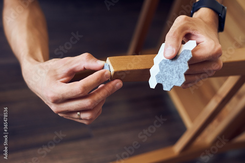 Sticking a floor care pad at wooden legs. Anti-skid felt pad cover install on wooden furniture leg. Floor protector.