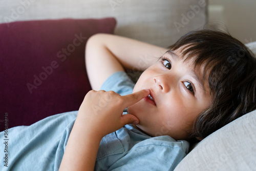 Happy kid boy putting fingers in his mouth with curious face while watching TV, Adorable child relaxing at home on weekend,  Relax and cozy scene concept