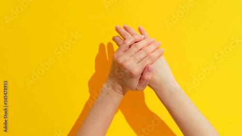 Hands of a woman who is rubbing her hands on a yellow background