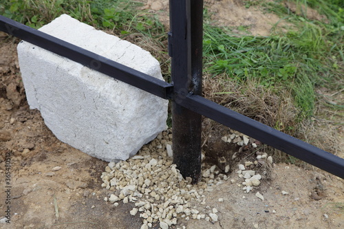 Installation of pillars supporting the welded base of a new metal fence, strengthening with gravel