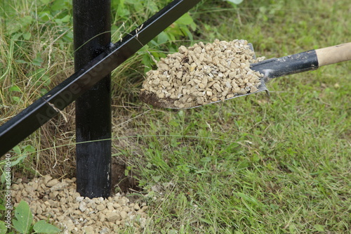 White grit on a shovel, strengthening with gravel of columns of supports of the base of a new metal fence