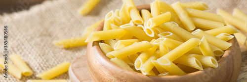 Penne pasta. Raw Penne Pasta in a wooden bowl on a brown wooden table. Banner with space for text