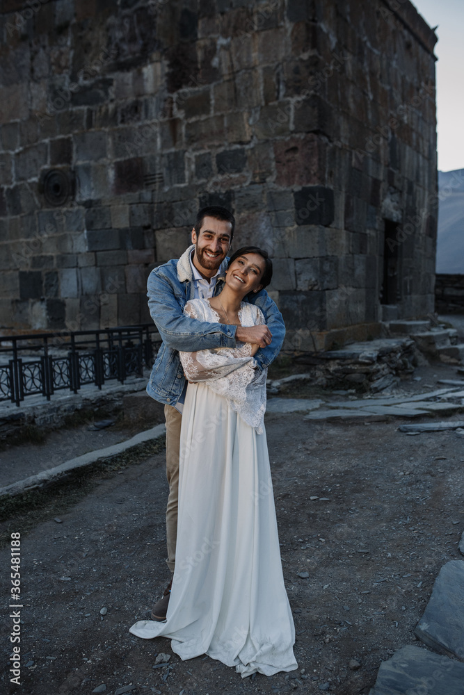 Young Georgian couple posing in the mountains. Boho wedding in Georgia. Evening setting sun. Blue jeans jacket