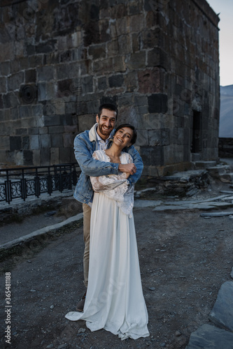 Young Georgian couple posing in the mountains. Boho wedding in Georgia. Evening setting sun. Blue jeans jacket © Denys