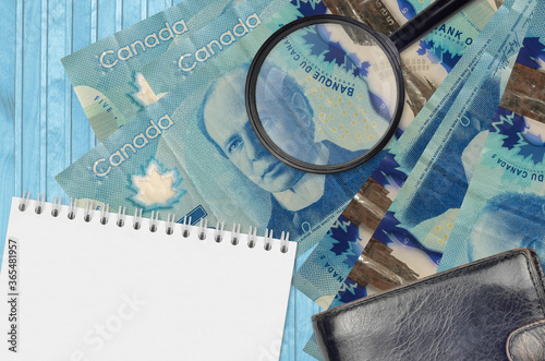5 Canadian dollars bills and magnifying glass with black purse and notepad. Concept of counterfeit money. Search for differences in details on money bills to detect fake