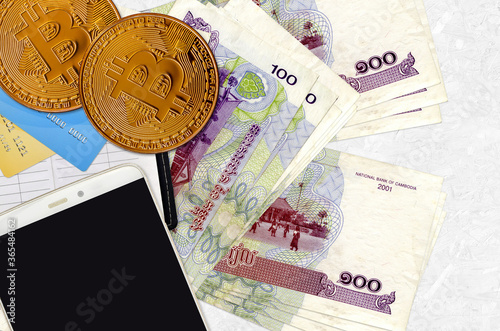 100 Cambodian riels bills and golden bitcoins with smartphone and credit cards. Cryptocurrency investment concept. Crypto mining or trading photo