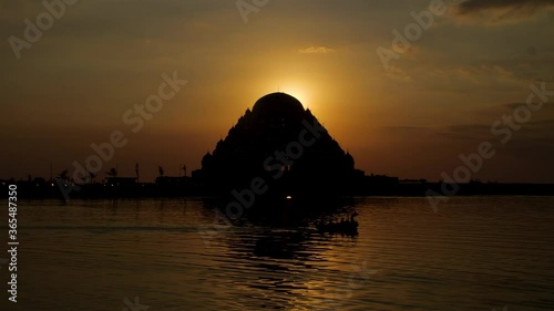 The sun setting behind the 99 domes mosque with a boat passing in the foreground photo