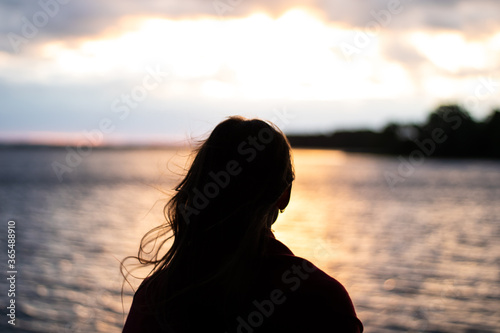 Silhouette of a girl at sunset on the lake. Girl watching the sunset over the lake