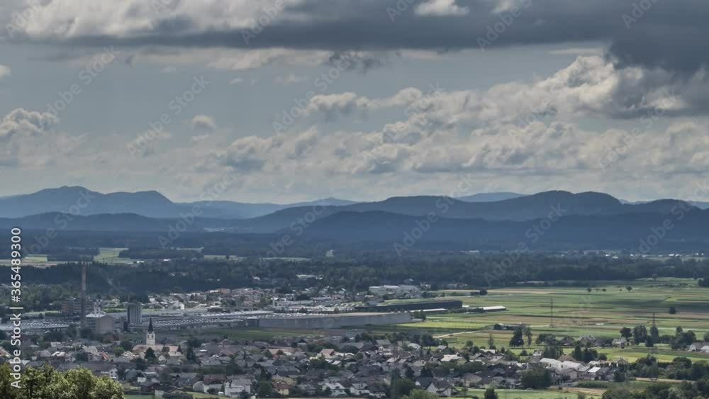 Time lapse clouds moving over Ljubljana basin flatland on bright sunny day. Houses and large factory in foreground, hills in background. Zoom out, aerial view Time lapse clouds moving over Ljubljana basin flatland on bright sunny day. Houses and large factory in foreground, hills in background. Zoom out, aerial view