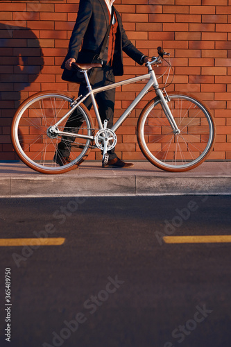 Crop businessman with bike walking on pavement