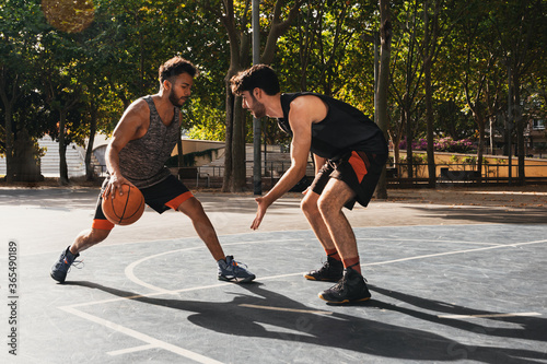 two young men playing basketball outdoors fight for the ball