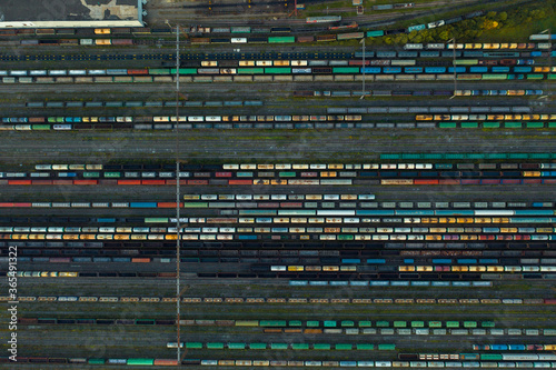 Aerial view of colorful freight trains on the railway station. Wagons with goods on railroad. Heavy industry. Industrial conceptual scene with trains. Top view from flying drone