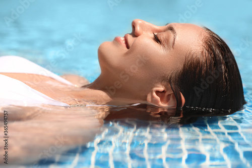 Beautiful young woman relaxing in outdoor swimming pool