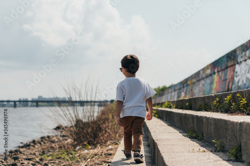 Fototapeta Naklejka Na Ścianę i Meble -  Back view of cute boy walking near river